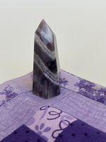 Load image into Gallery viewer, Alternate view. Chevron amethyst tower with the coolest banding for your altar, for healing or as décor for any room in your home or office. Amethyst, one of the most spiritual gemstones, heals, cleanses &amp; calms, allowing you to reach meditative &amp; higher consciousness levels more easily. It also helps to dispel negative emotional states and more. Chevron amethyst is a combination of amethyst and white quartz and when you add the quartz you get additional qualities. Approx. 2¼&quot; long. Cost is $13.20.
