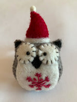 Load and play video in Gallery viewer, This close-up view of the Santa-hat owl Christmas ornament is handmade (fair trade) from 100% hand-felted wool. It is off-white and brownish-gray with some black accents (beak, ears, etc.) and wears an off-white and red Santa hat. The &#39;signature&#39; (red) snowflake is displayed on its chest/belly area. It is approximately 4.5&quot;x3&quot; and comes with a detachable fair trade holiday &quot;to/from&quot; tag to use if giving as a gift. 

