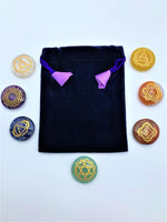 Load image into Gallery viewer, Chakra stone set includes 7 gemstone disks, each with the chakra symbol in gold. The stones included are: clear quartz, amethyst, sodalite, aventurine, yellow onyx, carnelian and red jasper - one stone for each of the major chakras. The set comes with a satin-lined velvet bag for storage. Use these stones during meditation or to cleanse, activate or align your chakras. These are natural stones and will vary in color from set to set. 
