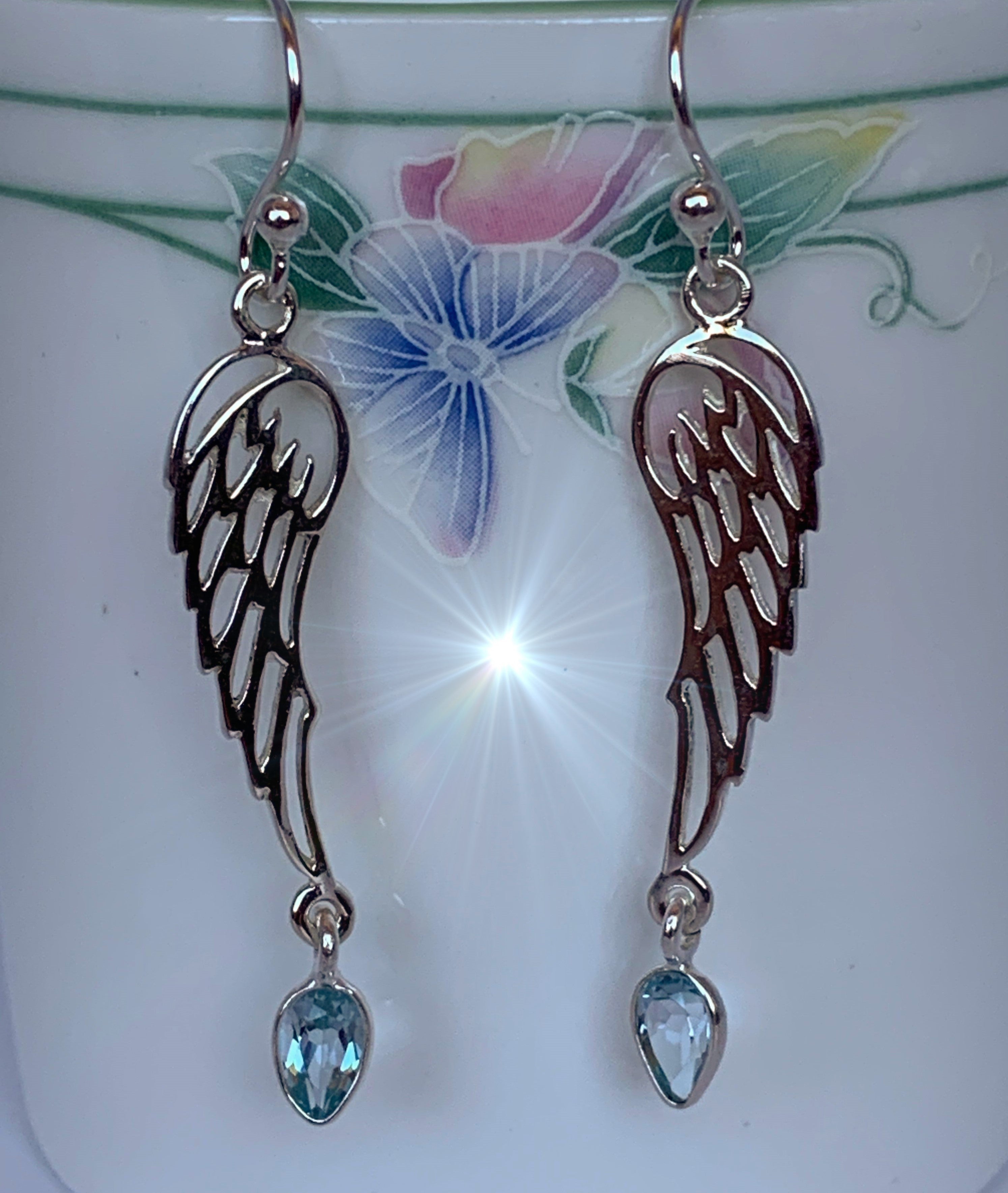  Close-up view. Pear shaped blue topaz dangle from open sterling silver angel wings. These earrings are lightweight, have wires, not posts for wearing and are approximately 1 ¾" long.