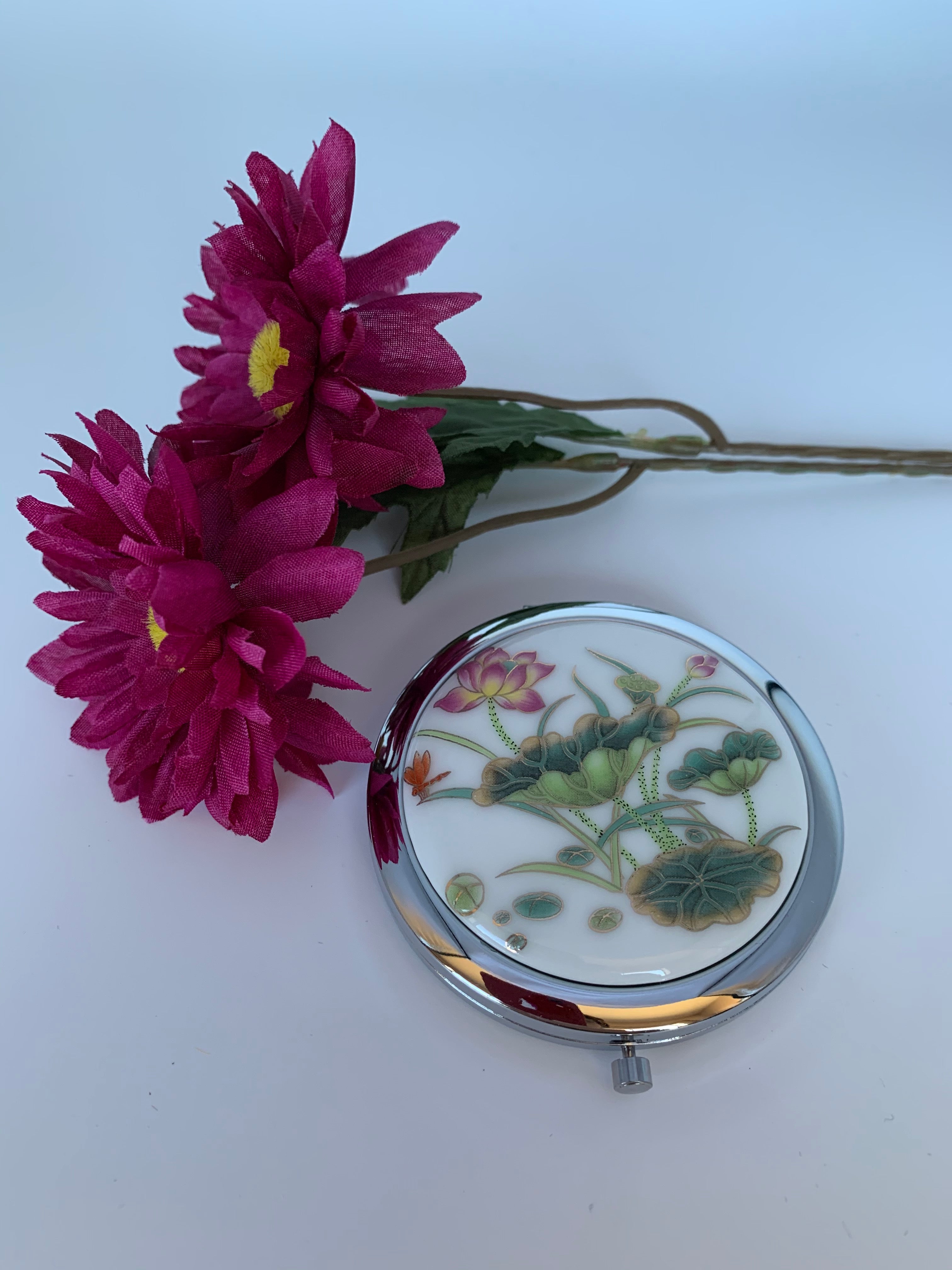 Second view. Great little compact mirror for purse or vanity. It is hinged with 2 mirrors.Aand the lotus adds a beautiful and spiritual touch. It is functional and also elegant. I keep mine out on my bathroom counter because it is so pretty to look at. The lotus flower is a sacred symbol reminding us that we all must push through the mud to get to the light. It stands for purity, strength and enlightenment. It is approximately 2¾" across. Great gift, great price - $5.00.