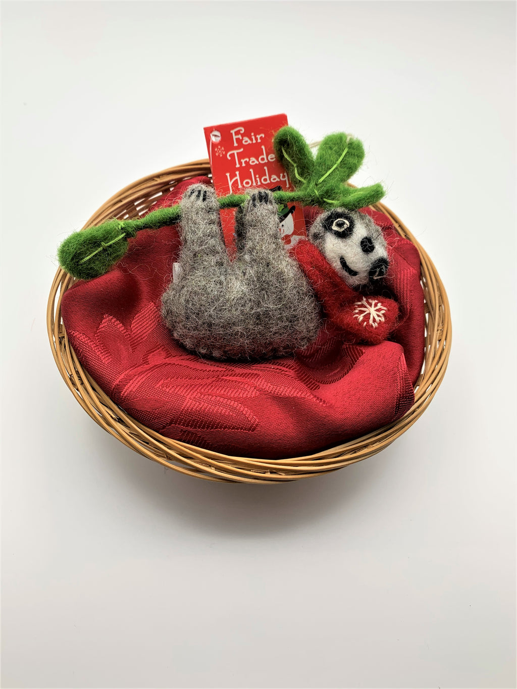 This sloth Christmas ornament is hand-crafted (fair trade) and made of 100% natural wool.  It is brownish-gray with an off-white face, with black accents (nose, mouth, etc) and is wearing a red winter scarf with the 'signature' (white) snowflake on it.  It is hanging from a green branch with green leaves. Approximately 4.75"x4.25". It comes with a detachable fair trade "to/from" tag to use if giving as a gift.