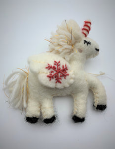 This is a close-up photo of a unicorn Christmas ornament that is hand-crafted (fair trade) and made of 100% natural wool. It is off-white with a red and white striped horn, golden threads within its mane, has black accents (hooves, mouth, etc.) and has the 'signature' (red) snowflake on it's wing. It is approximately 5"x4" (with the tail being extra 1.5"). It comes with a detachable fair trade holiday "to/from" tag to be used if giving as a gift.