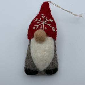 This is a closeup photo of the gnome Christmas ornament and is handcrafted (fair trade) and made of 100% natural wool. It has a brownish-gray body, a long white beard, a round nose and a pointed red hat with the 'signature' (white) snowflake on it and there are no visible eyes as the hat covers that area. Approximately 5.5"x2.5" and comes with a detachable fair trade holiday "to/from" tag to use if you are giving this as a gift.