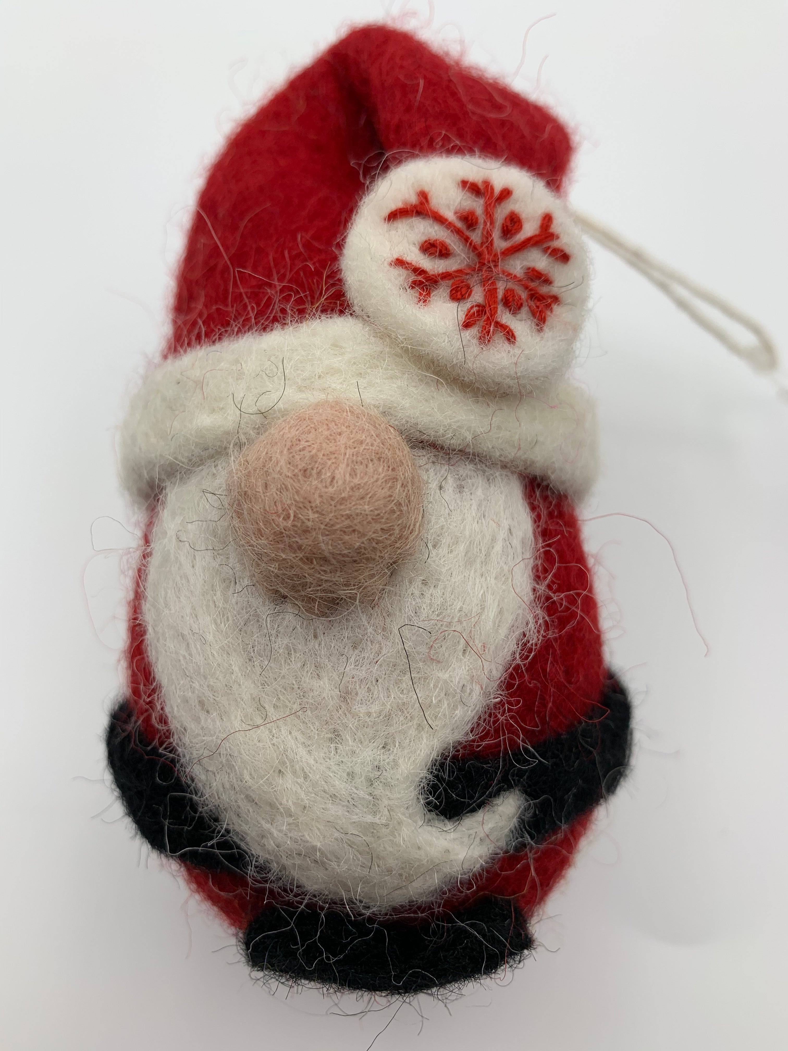 This is a close-up photo of the Santa Claus Ornament that is handcrafted (fair trade) and made with 100% natural wool. He has a red body and a red hat with white trim, a long beard, a round nose and black accents (belt and feet/boots). Approximately 4"x2.25". He comes with a fair trade holiday "to/from" tag to use if giving this as a gift.