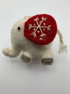 This is a close-up photo of Jumbo the elephant, a Christmas ornament that is hand-crafted (fair trade) and is made of 100% natural wool. He is off-white with large red ears and black accents (feet, eyes, etc.). The 'signature' (white) snowflake is on his ear. He is approximately 3"x3.25" (his tail adds another 1.75"). He comes with a fair trade holiday "to/from" tag to use if giving this as a gift.