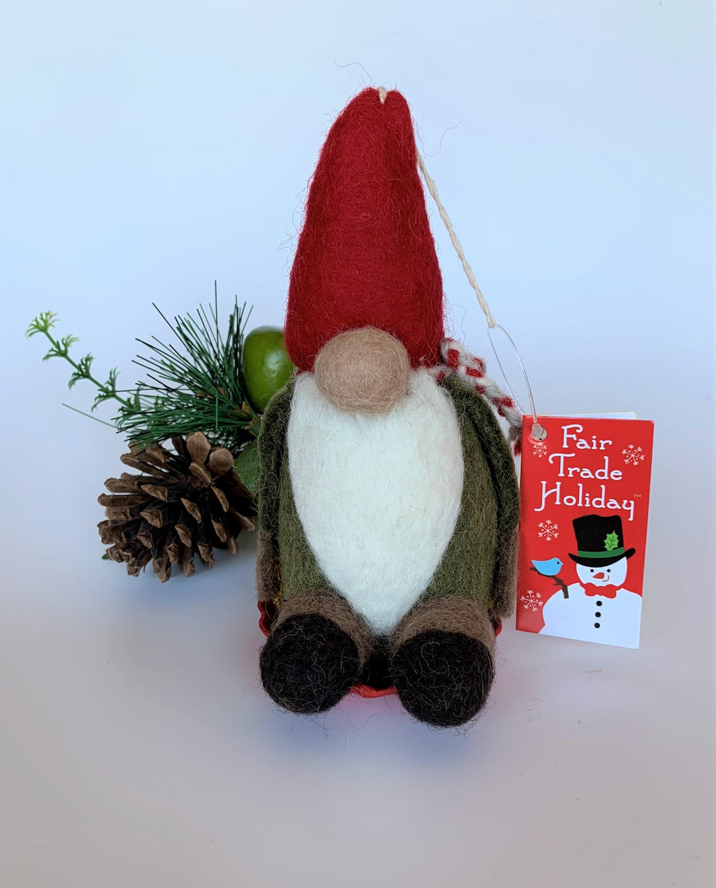 This is the sledding gnome Christmas ornament that is handcrafted (fair trade) and made of 100% natural wool. The sled is handmade using paper that is hardened & feels almost like thin wood. He wears a green top, brownish-gray pants, a pointed red hat, which covers his eyes, a red & white scarf, has a round tan nose & sits on a round, red sled with gold colored sled handles on either side. Approximately 6.5"x3.75"x3.5". He comes with a fair trade holiday "to/from" tag to use if giving this as a gift.