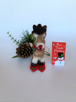 Load image into Gallery viewer, This is a skiing Rudolph the red-nosed reindeer Christmas ornament that is handcrafted (fair trade) from 100% natural wool. He is  off-white and brown with brown ears and tail, dark brown antlers, black accents (feet, mouth, etc.) and a red nose. He wears a red and green winter scarf with an accent of holly and  stands on a pair of red skis with green accents on the front. Approximately 3.5&quot;x1.5&quot;x1.75&quot;.  He comes with a detachable fair trade holiday &quot;to/from&quot; tag to use if giving as a gift.
