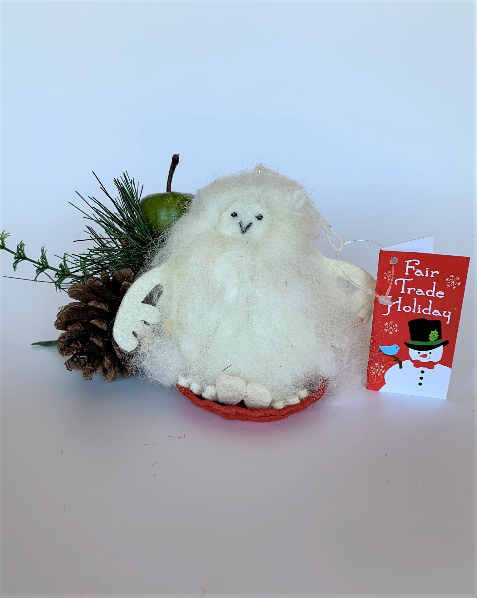 This is a sledding Yeti Christmas ornament that is handcrafted (fair trade) and made of 100% natural wool. The sled is handmade using paper that is hardened and feels almost like thin wood.  It is off-white with black accents (eyes and mouth), with off-white felted arms and feet. It sits on a round, red sled with gold colored "rope" handles  on either side.  Approximately 4.5"x2.75"x2.75".  It comes with a detachable fair trade holiday "to/from" tag to use if giving this as a gift.