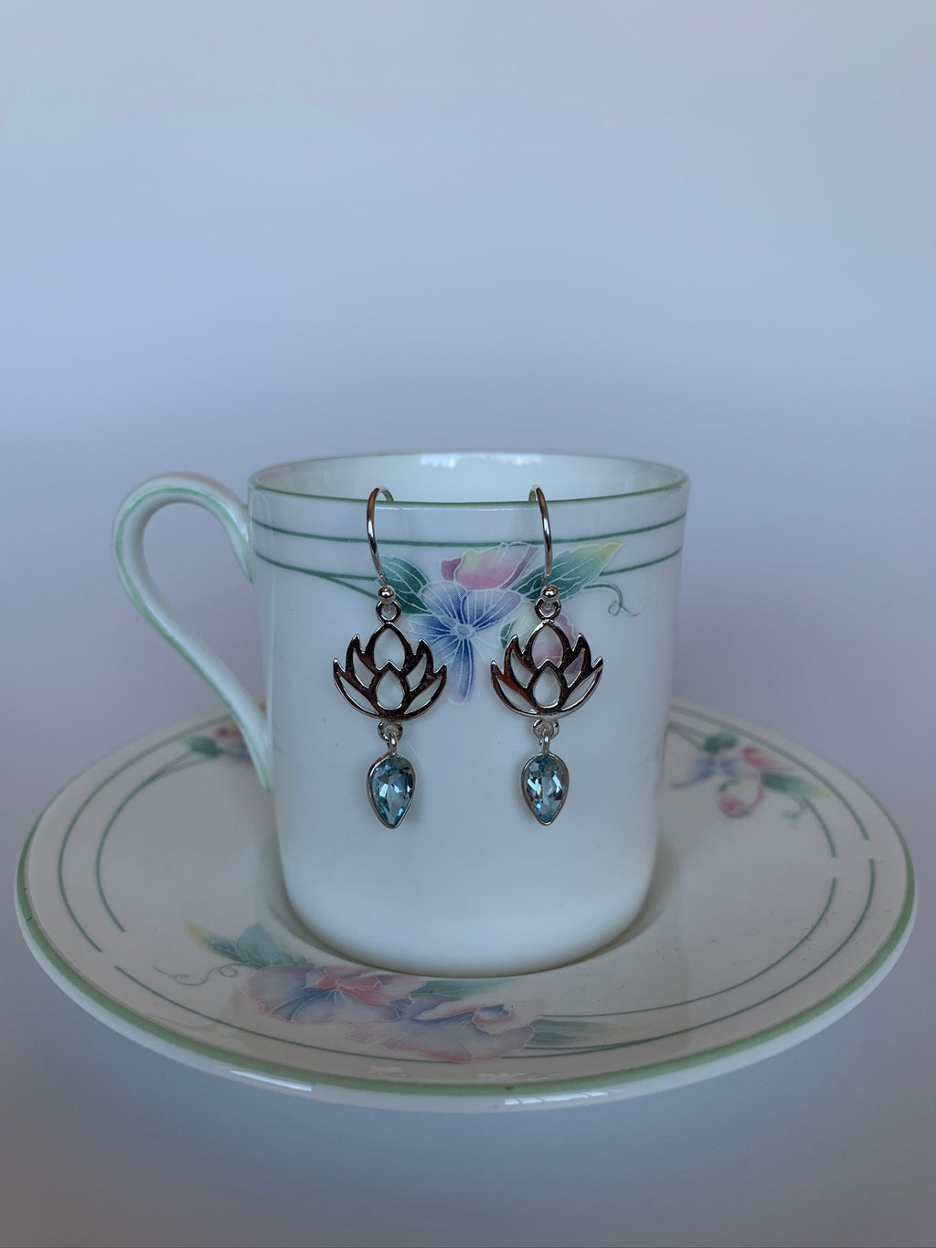 Sterling silver earrings with earring wires, not posts.  A blue topaz (reverse teardrop) hangs from a sterling silver lotus design. Earrings are lightweight and are approximately 1½" long.