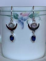 Load image into Gallery viewer, Close up view. These gorgeous &amp; lightweight sterling silver earrings consist of a sterling upturned crescent moon with a small round moonstone within its curve and a blue oval faceted kyanite gemstone hanging below it. Wires, not posts for wearing. Approximately 1½&quot; long.
