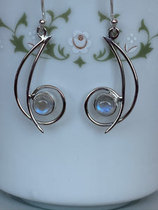 Close-up view. These sterling silver earrings have open (stylized) crescent moons with a sterling circle at the bottom, holding a small round moonstone. They are lightweight and approximately 1¾" long.