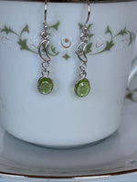 Load image into Gallery viewer, Close-up view. Small round peridot gemstones dangle from little open sterling silver crescent moons. Wires, not posts for wearing. Approximately 1½&quot; long.
