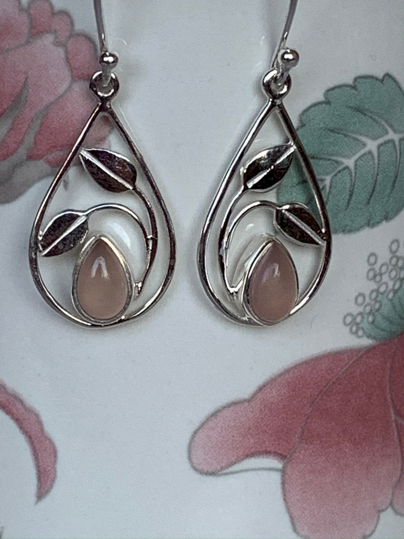 Close-up view, teardrop pink Chalcedony set in sterling silver at the bottom of an open sterling silver teardrop shape with sterling silver "swaying" leaves above. Wires, not posts. These earrings are lightweight and approximately 1¼" long.