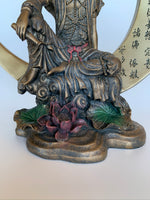 Load image into Gallery viewer, Close-up View of bottom of the beautiful, detailed statue of Kwan Yin sitting on a large crescent moon finished in a burnished bronze. Kwan Yin is a revered and powerful goddess. She symbolizes compassion, mercy and kindness. The moon represents powerful feminine energy, intuition, emotions/feelings. Color is added to certain details on this lovely statue, adding to its appeal. Red and green are added to the lotus flower and leaves below her and red is added to her belt &amp; forehead. Approximately 7¾&quot; tall.
