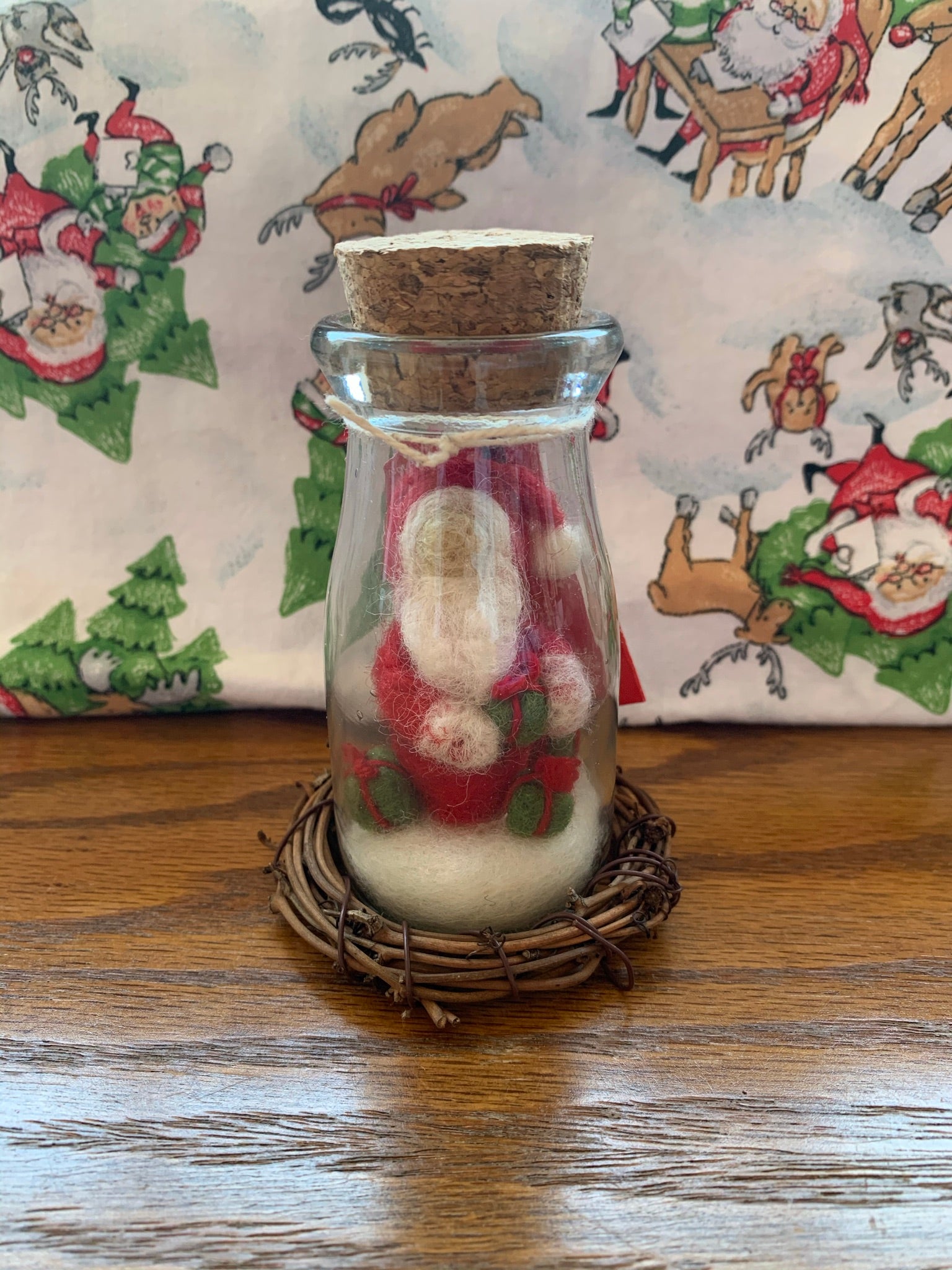 This is a story jar Santa Christmas Ornament. A corked, apothecary jar holds Santa sitting on the snow holding a gift and with two other gifts on the snow around him.  He wears the traditional Santa colors of red & white and wears white woolen mittens.  He is made of 100% natural, hand-felted wool and is approximately 4.5"x2". He comes with a fair trade home & garden tag.
