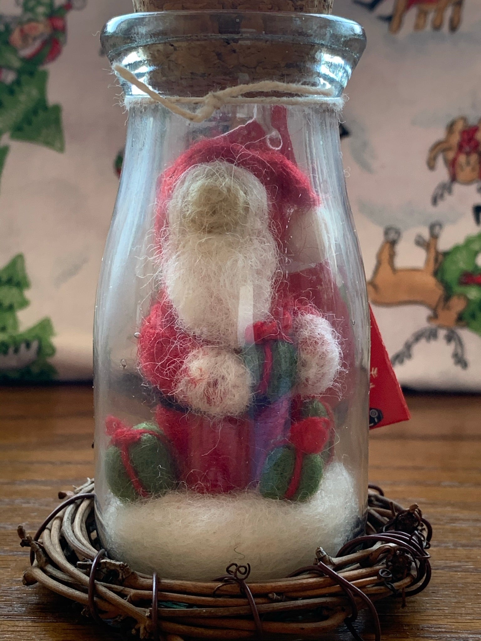 This is a story jar Santa Christmas Ornament. A corked, apothecary jar holds Santa sitting on the snow holding a gift and with two other gifts on the snow around him. He wears the traditional Santa colors of red & white and wears white woolen mittens. He is made of 100% natural, hand-felted wool and is approximately 4.5"x2". He comes with a fair trade home & garden tag.