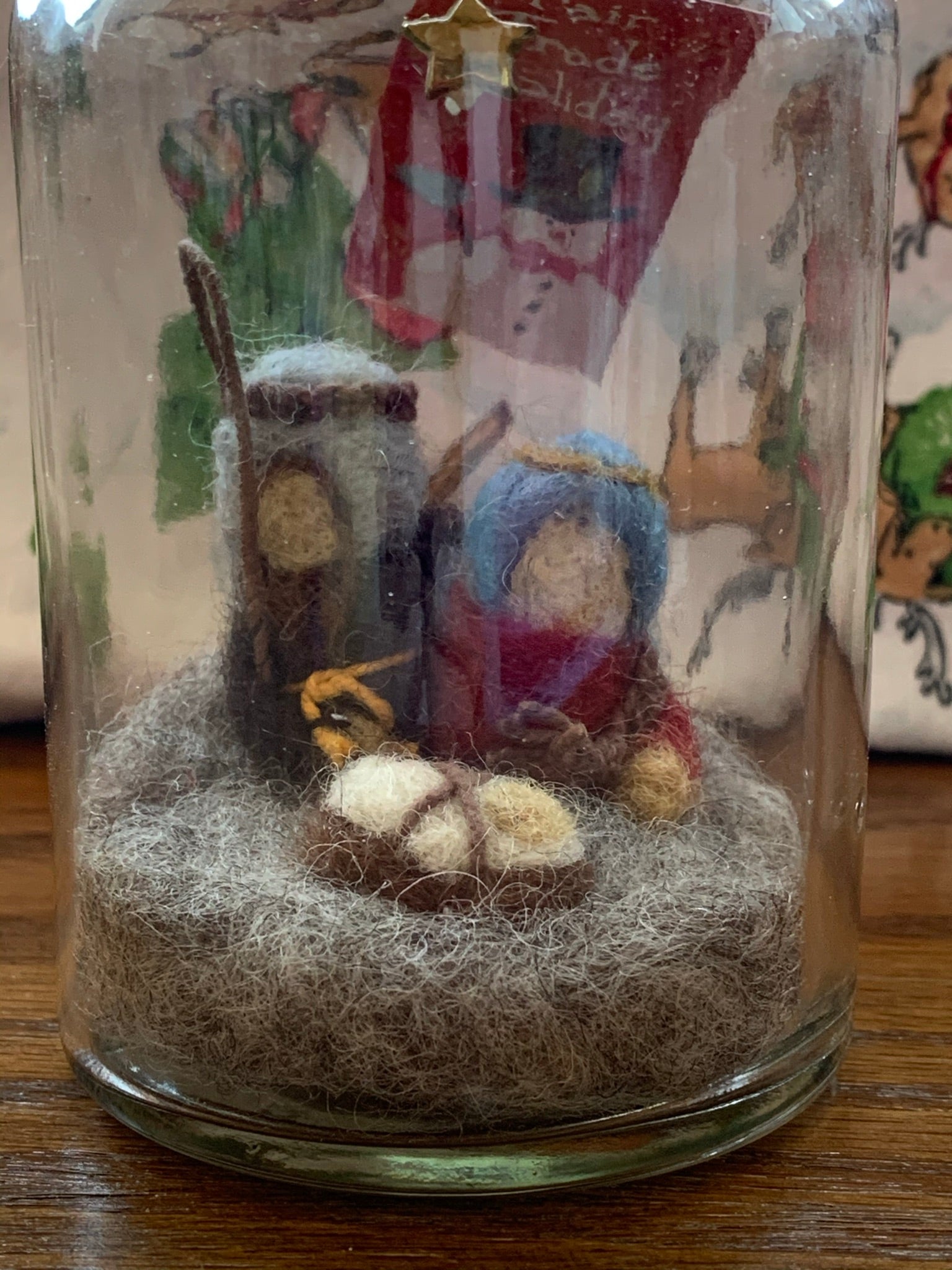 This close-up of the Nativity story jar Christmas ornament displays Mary, Joseph and baby Jesus with a star above them, sitting on the ground. They sit inside a corked apothecary bottle. The Nativity is made of 100% natural wool. The bottle is affixed with a metal wire for hanging, but can also be placed on a shelf or table top. Approximately 3"x1" (6.75" if you include the wire hanger). It comes with a fair trade home and and garden tag.