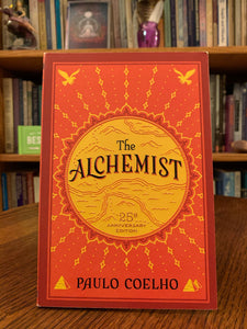 Front cover. The Alchemist - 25th Anniversary edition. This is an extraordinary international best-seller. It is a tale that takes one Andalusian shepherd boy, Santiago, on an adventure to find treasure near a pyramid, but the treasure he truly finds is not worldly treasure, but one much more important and satisfying - the treasure of self-discovery, of following is own heart, the signs along the way and of discovering his true dream. Cost is $16.99. Book purposely produced with rough cut edges.