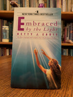 Load image into Gallery viewer, Close-up of front cover. Embraced by the Light is the true story of Betty J. Eadie&#39;s amazing, profound, and life-changing near death experience. It is detailed and mind-blowing and as you walk through her story with her you will be inspired by her experience! She came away with the idea that she often shares - &quot;That death need not be feared&quot; and that the spirit world is one of exquisite beauty. Cost is $7.99
