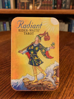 Load image into Gallery viewer, This Radiant Rider-Tarot Deck, takes the traditional illustrations up a notch with enhanced brightness and a lovely new card back, now illustrated with a deep blue, star-filled sky. If you like the traditional tarot, this is the deck for you. The set includes 78 cards, a guide booklet, and a tin for storage (instead of the regular cardboard box). Price is $18.95. This photo is of the front of the storage tin.
