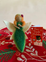 Load image into Gallery viewer, This earth fairy Christmas ornament is handmade (fair trade) from 100% wool. She is tan skinned &amp; wearing a dark green dress with light green on the edge &amp; has a double row of tiny green beads around the empire waist. She wears a light green hat with a red flower on it, has orange hair and white wings with a bit of light yellow on them.  She has bendable arms and no facial markings.  She is approximately 5&quot;x2.5&quot; and comes with a fair trade holiday &quot;to/from&quot; tag to use if giving as a gift.
