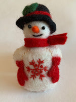 Load image into Gallery viewer, This Snowman Christmas ornament is handmade (fair trade) from 100% hand-felted wool. It is off-white with some black accents (eyes, mouth) and wears a black top-hat with red &amp; green accents and red woolen mittens and scarf. It has a orange carrot shaped nose and the &#39;signature&#39; (red) snowflake is displayed on its belly. It is approximately 4.5&quot;x2.75&quot; and comes with a detachable fair trade holiday &quot;to/from&quot; tag to use if giving as a gift. 
