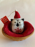 Load image into Gallery viewer, This Santa-hat owl Christmas ornament is handmade (fair trade) from 100% hand-felted wool. It is off-white and brownish-gray with some black accents (beak, ears, etc.) and wears an off-white and red Santa hat. The &#39;signature&#39; (red) snowflake is displayed on its chest/belly area. It is approximately 4.5&quot;x3&quot; and comes with a detachable fair trade holiday &quot;to/from&quot; tag to use if giving this as a gift. 
