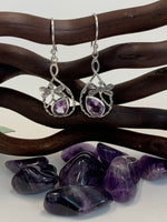 Load image into Gallery viewer, Teardrop shaped amethyst set, at a slant, at the bottom of an open tear drop shaped silver loop. sterling silver dragonflies &quot;fly&quot; above the amethysts. These beautiful and fanciful earrings are lightweight, have wires, not posts and are approximately 1½&quot; long. 
