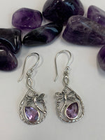 Load image into Gallery viewer, Close-up view. Teardrop shaped amethyst set, at a slant, at the bottom of an open tear drop shaped silver loop. sterling silver dragonflies &quot;fly&quot; above the amethysts. These beautiful and fanciful earrings are lightweight, have wires, not posts and are approximately 1½&quot; long
