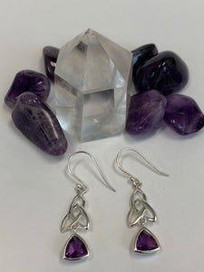 Close-up view. Trilliant cut (triangular) faceted amethyst gemstones outlined in sterling silver, dangle from an elongated Celtic trinity knot, or triquetra. These earrings are lightweight, have wires, not posts and are approximately 1½" long.