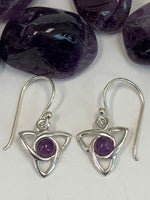 Load image into Gallery viewer, Close-up view. Round amethyst gemstones (cabs, not faceted) sit in the middle of a sterling silver Celtic trinity knot (or triquetra). These earrings are lightweight, have wires, not posts and are approximately 1¼&quot; long.
