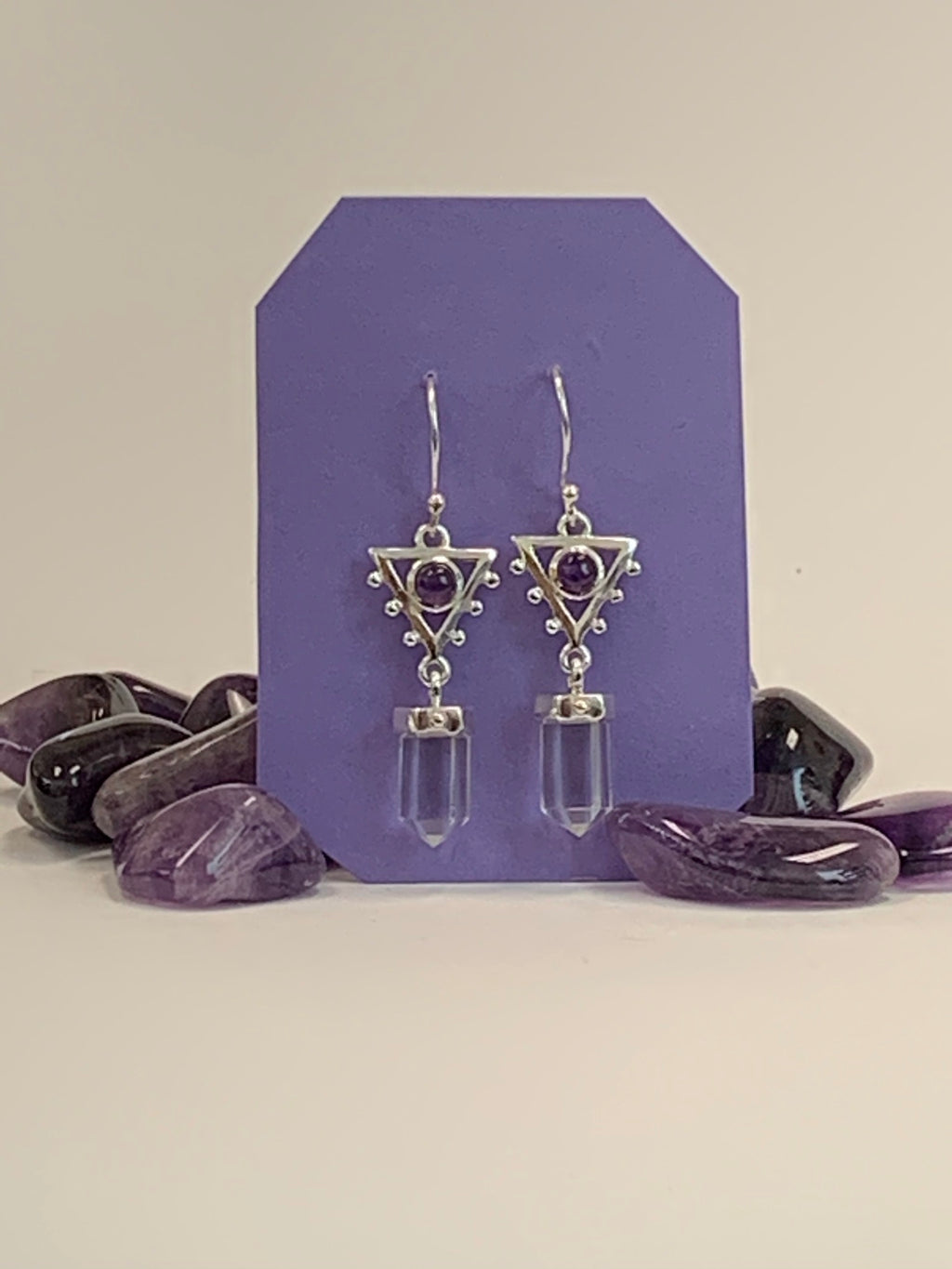 Small, round amethyst gemstones (cabs, not faceted) sit within a sterling silver upside-down triangle with tiny balls of silver lining two sides of the triangle. Clear quartz crystal points dangle below the triangle. These beautiful earrings have wires, not posts and are approximately 1½" long.
