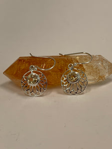 Close-up view. Round, faceted citrine gemstones are set at the top of an open sterling silver lotus flower, which itself is set in a circle of sterling silver. These earrings are lightweight, have wires, not posts and are approximately 1½" long.