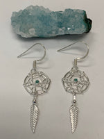 Load image into Gallery viewer, Close-up view. Tiny turquoise gemstones are set in the middle of a round dreamcatcher with a silver feather hanging beneath it. These earrings are very delicate, sweet and lightweight. They have wires, not posts and are approximately 1½&quot; long.
