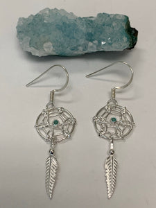 Close-up view. Tiny turquoise gemstones are set in the middle of a round dreamcatcher with a silver feather hanging beneath it. These earrings are very delicate, sweet and lightweight. They have wires, not posts and are approximately 1½" long.