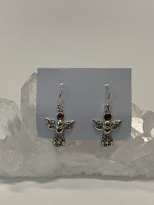 Small, round, faceted garnet gemstones are outlined in sterling silver and set above an angel's wings and dress (the garnet is in place of the angel's head/face). The angel's body and wings are filled with swirls of silver and there is a solid silver heart on the body, beneath the wings. This is a small and delicate pair of earrings. They are lightweight, have wires, not posts and are approximately 1½" long. 