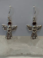 Load image into Gallery viewer, Close-up view. Small, round, faceted garnet gemstones are outlined in sterling silver and set above an angel&#39;s wings and dress (the garnet is in place of the angel&#39;s head/face). The angel&#39;s body and wings are filled with swirls of silver and there is a solid silver heart on the body, beneath the wings. This is a small and delicate pair of earrings. They are lightweight, have wires, not posts and are approximately 1½&quot; long.
