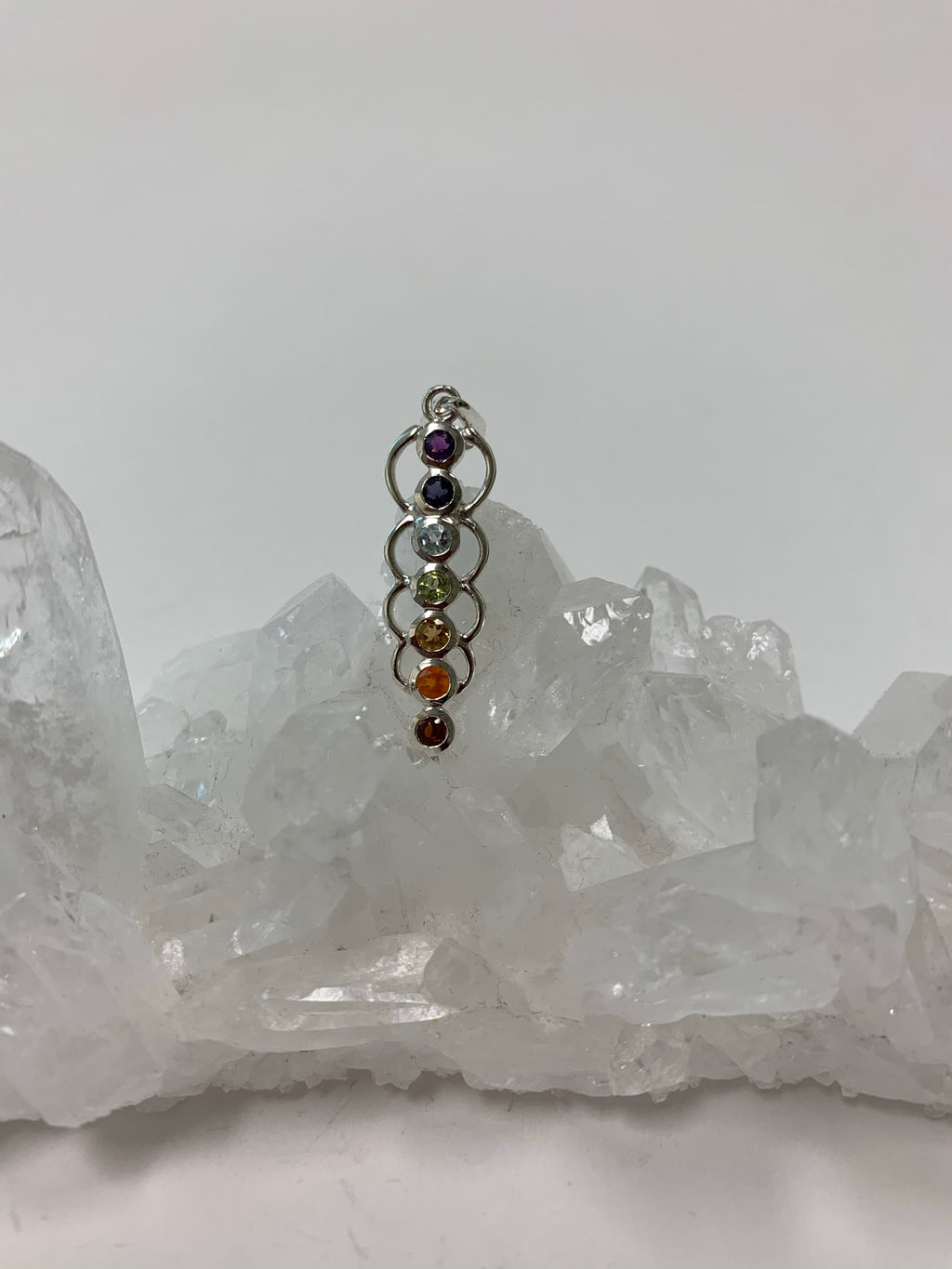 Chakra energy link pendant. Small faceted stones that represent each of the chakras: amethyst/crown, iolite/third eye, blue topaz/throat, peridot/heart, citrine/solar plexus, carnelian/sacral (or naval), garnet/root (or base). These stones, set in links or loops of sterling silver, two per loop or link, go straight down the middle. Pendant is approximately 1¾".