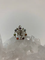 Load image into Gallery viewer, Chakra fairy pendant. Small faceted stones represent each of the chakras: amethyst/crown, iolite/third eye, blue topaz/throat, peridot/heart, citrine/solar plexus, carnelian/sacral (or naval), garnet/root (or base). These small, faceted stones are set around an open sterling silver circle. A sterling silver fairy extends through the center of the circle. Her wings reach a bit beyond the top of the circle and her feet touch the bottom. Pendant is approximately 1&quot;.
