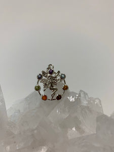 Chakra fairy pendant. Small faceted stones represent each of the chakras: amethyst/crown, iolite/third eye, blue topaz/throat, peridot/heart, citrine/solar plexus, carnelian/sacral (or naval), garnet/root (or base). These small, faceted stones are set around an open sterling silver circle. A sterling silver fairy extends through the center of the circle. Her wings reach a bit beyond the top of the circle and her feet touch the bottom. Pendant is approximately 1".
