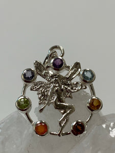 Close-up view. Chakra fairy pendant. Small faceted stones represent each of the chakras: amethyst/crown, iolite/third eye, blue topaz/throat, peridot/heart, citrine/solar plexus, carnelian/sacral (or naval), garnet/root (or base). These small, faceted stones are set around an open sterling silver circle. A sterling silver fairy extends through the center of the circle. Her wings reach a bit beyond the top of the circle and her feet touch the bottom. Pendant is approximately 1".