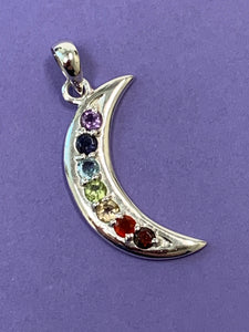 Close-up view of the Chakra crescent moon pendant. Small faceted stones represent each of the chakras: amethyst/crown, iolite/third eye, blue topaz/throat, peridot/heart, citrine/solar plexus, carnelian/sacral (or naval), garnet/root (or base). These small, faceted stones are set, in a curve, along a solid sterling crescent moon. Pendant is approximately 1¼".