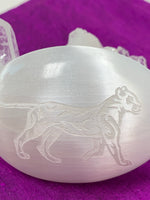 Load image into Gallery viewer, Close up view of the lioness etched on a white, polished selenite palm stone from our spirit animal collection. Lioness embodies the goddess &amp; divine feminine and is related to The Great Mother. She is also seen as a protector, provider and as resourceful. She is the nurturer and fierce protector. The selenite ranges from translucent to milky white depending on the stone. Selenite is sourced ethically and workers are paid living wages.
