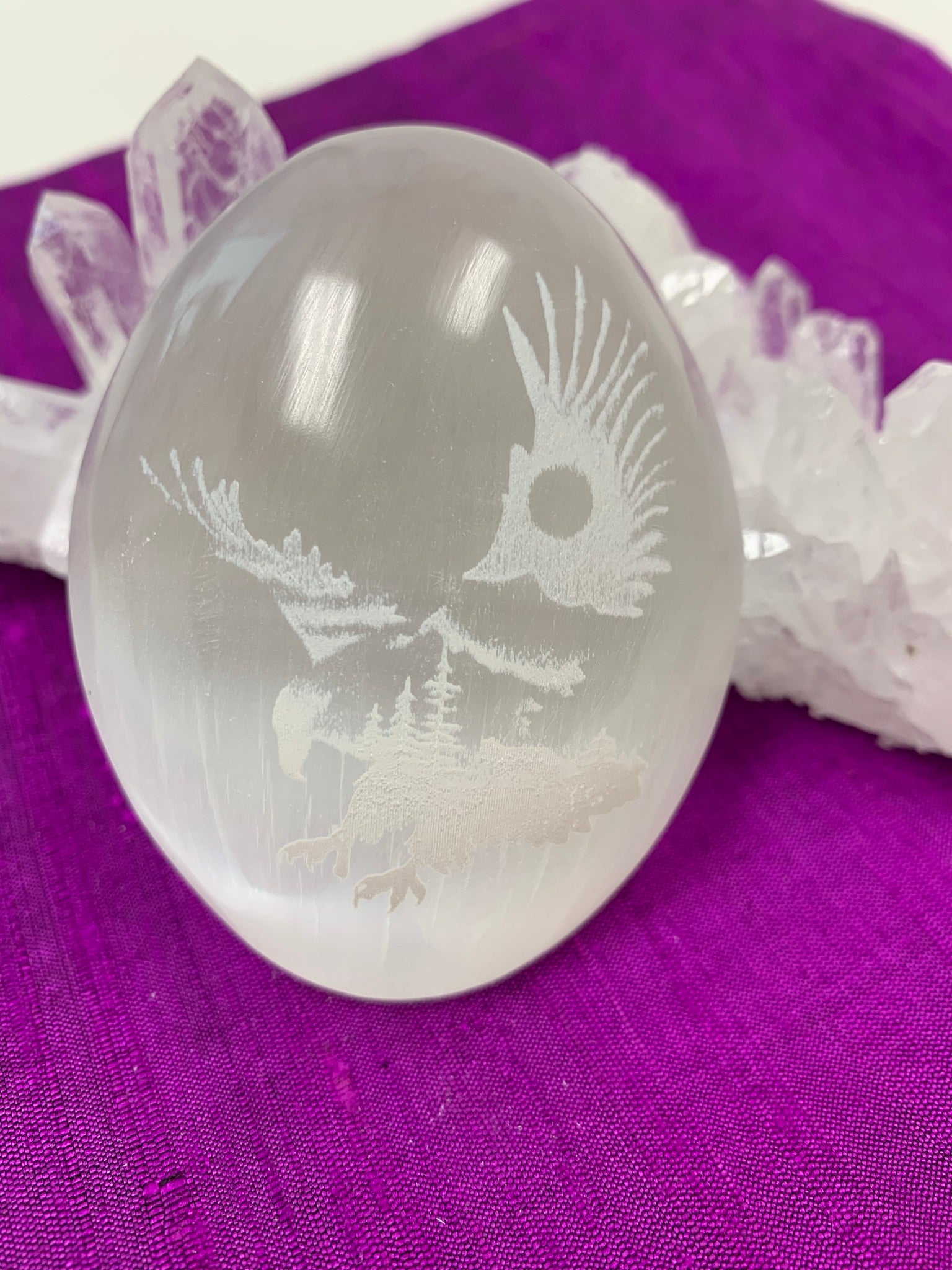 Eagle etched on white selenite palm stone. Selenite can range from translucent to milky white. Eagle is joined with the earth in this etching where the trees are a part of its body and the sun, a part of its wings. Average weight of these palm stones is 4.2 oz and they are approximately 3"x2.5", the perfect size to hold in the palm of your hand. These selenite stones are ethically sourced and workers are paid living wages. 