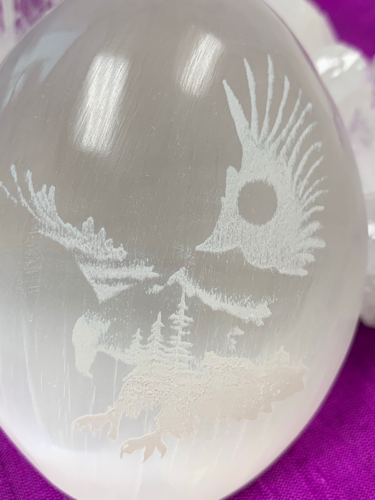 Close-up of the eagle etched on white selenite palm stone. Selenite can range from translucent to milky white. Eagle is joined with the earth in this etching where the trees are a part of its body and the sun, a part of its wings. Average weight of these palm stones is 4.2 oz and they are approximately 3"x2.5", the perfect size to hold in the palm of your hand. These selenite stones are ethically sourced and workers are paid living wages.