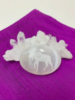 Load image into Gallery viewer, Moose etched on a smooth, polished selenite palm stone. The selenite ranges from translucent to milky white in color. Moose is associated with self-esteem, joyful sharing of a job well done and self acceptance and self-love. The palm stones vary in weight, but the average is 4.2 oz. The approximate size is 3&quot;x2.5&quot;. This selenite is ethically sourced and workers are paid living wages.
