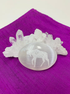 Moose etched on a smooth, polished selenite palm stone. The selenite ranges from translucent to milky white in color. Moose is associated with self-esteem, joyful sharing of a job well done and self acceptance and self-love. The palm stones vary in weight, but the average is 4.2 oz. The approximate size is 3"x2.5". This selenite is ethically sourced and workers are paid living wages.