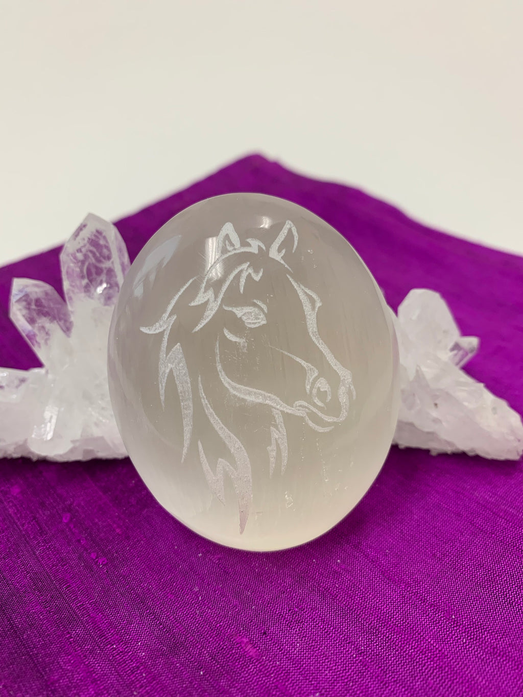Horse (head and mane) etched on smooth, polished white selenite. Selenite ranges from translucent to milky white in color. Horse represents power and the use of wisdom with power. These selenite stones vary in weight, but the average is 4.2 oz. and size is approximately 3"X2.5". These selenite stones are ethically sourced and workers earn living wages.  