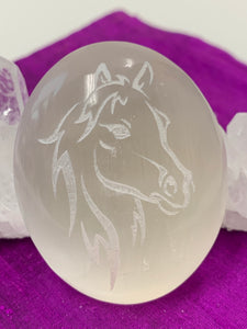Close-up of the horse (head and mane) etched on smooth, polished white selenite. Selenite ranges from translucent to milky white in color. Horse represents power and the use of wisdom with power. These selenite stones vary in weight, but the average is 4.2 oz. and size is approximately 3"X2.5". These selenite stones are ethically sourced and workers earn living wages.